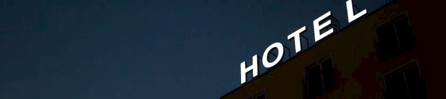 A building at night with a partially illuminated sign that reads "HOTEL" on its roof. The sign has a missing letter "E," making it read "HOT L."