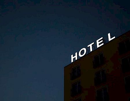 A building at night with a partially illuminated sign that reads "HOTEL" on its roof. The sign has a missing letter "E," making it read "HOT L."