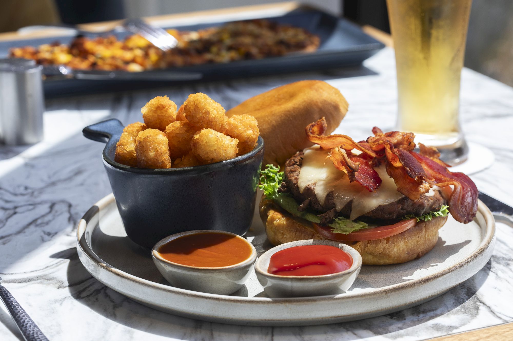 A bacon cheeseburger with crispy fries, served on a tray with ketchup and barbecue dipping sauce.