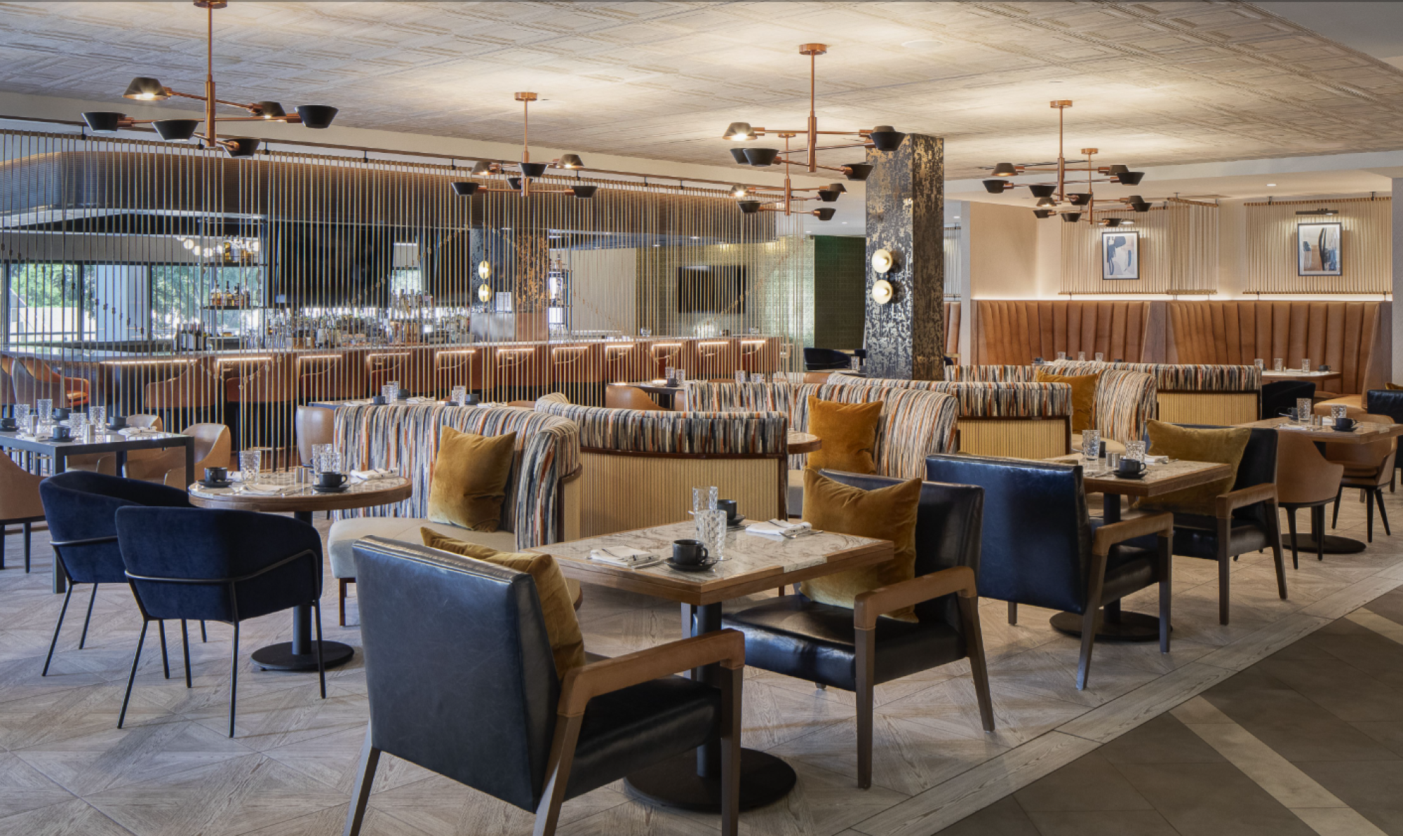 This image shows a modern, well-lit restaurant with stylish furniture, wooden tables, cushioned chairs, and a decorative ceiling.