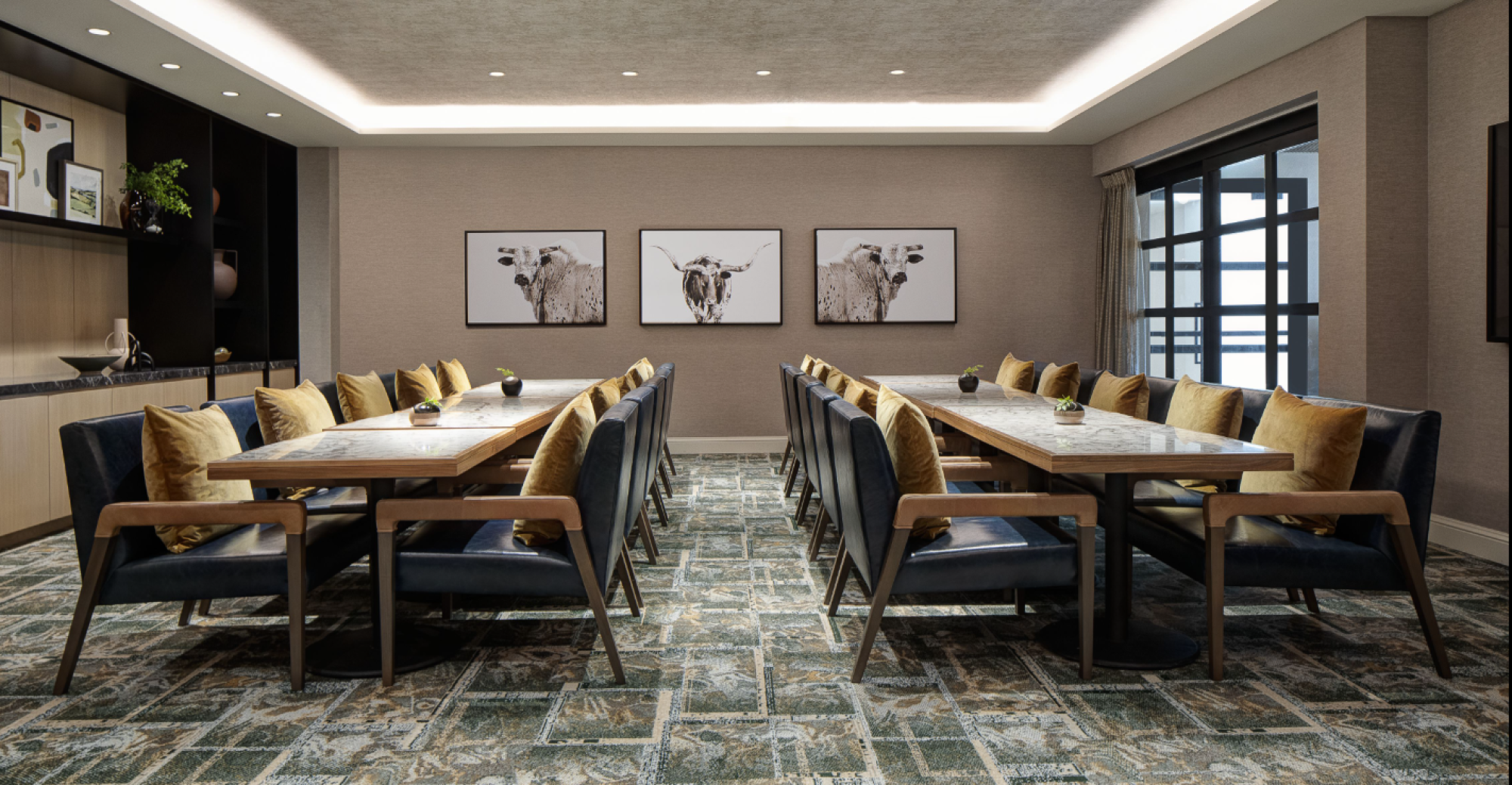 A modern conference room with two long tables, blue and mustard chairs, wall art with animal photos, and shelves with decorations.