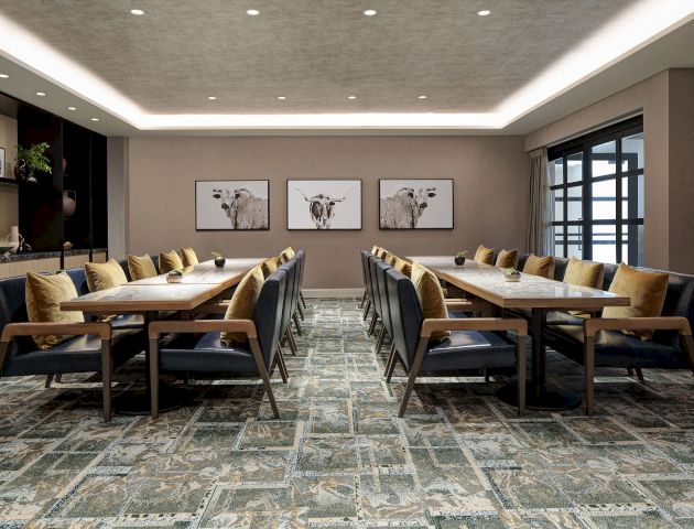 A spacious, modern conference room with a long table, cushioned chairs, decorative pillows, three bovine-themed art pieces, and a patterned carpet.