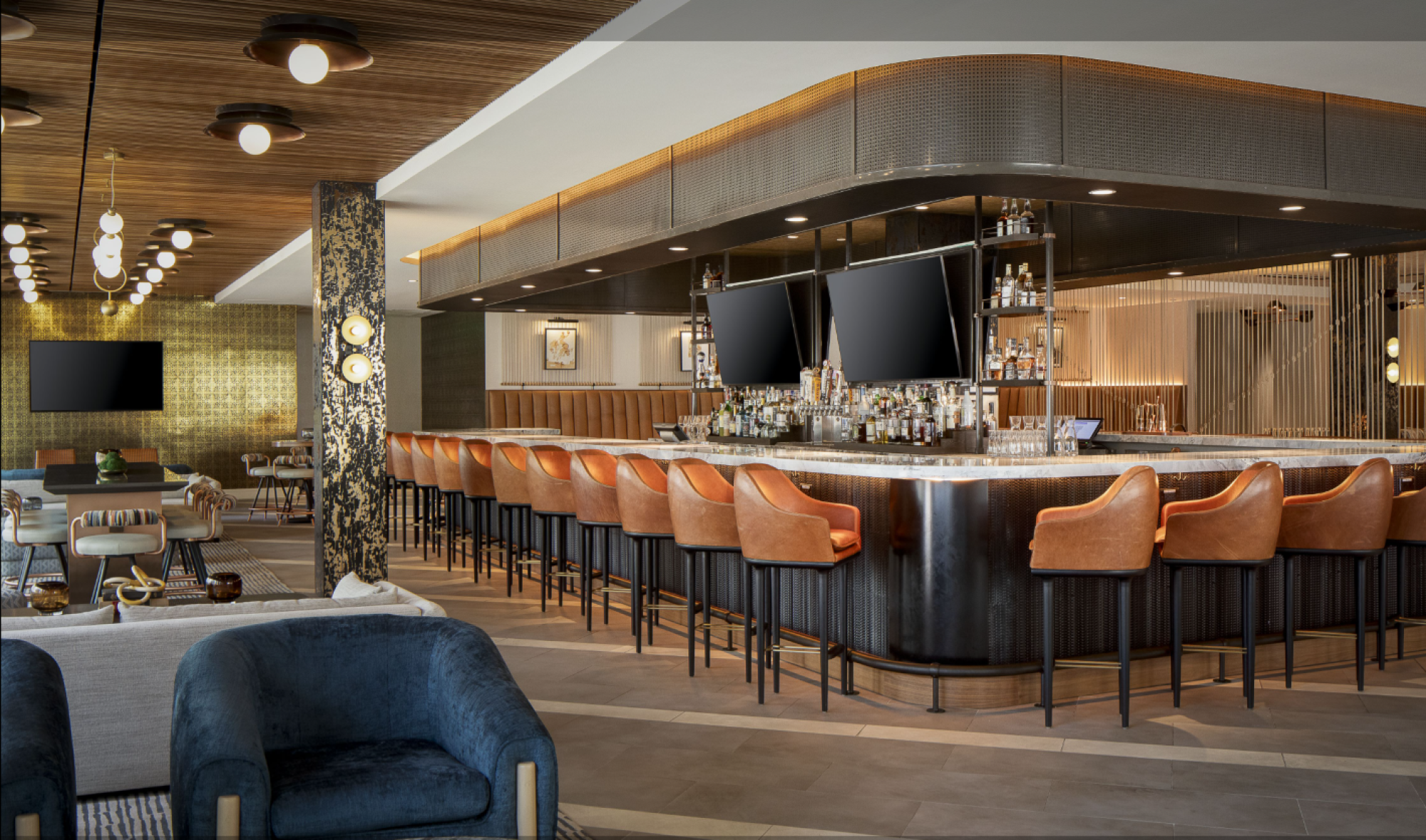 The image shows a modern bar with upholstered orange stools around the counter, large flat-screen TVs, and stylish lighting with additional seating in the background.