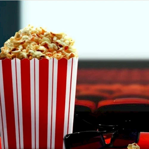 A striped popcorn box sits in a movie theater with red seats and a blurred screen in the background.