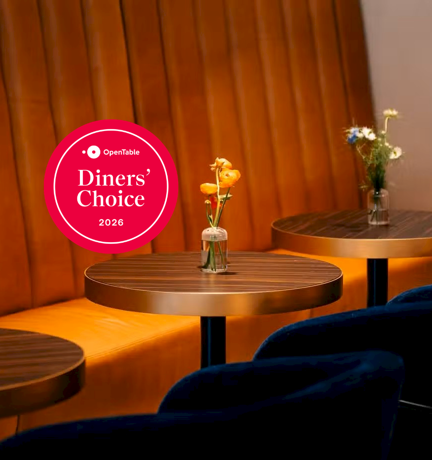 A cozy restaurant lounge with round tables, flower vases, and an OpenTable Diners&rsquo; Choice 2026 badge.